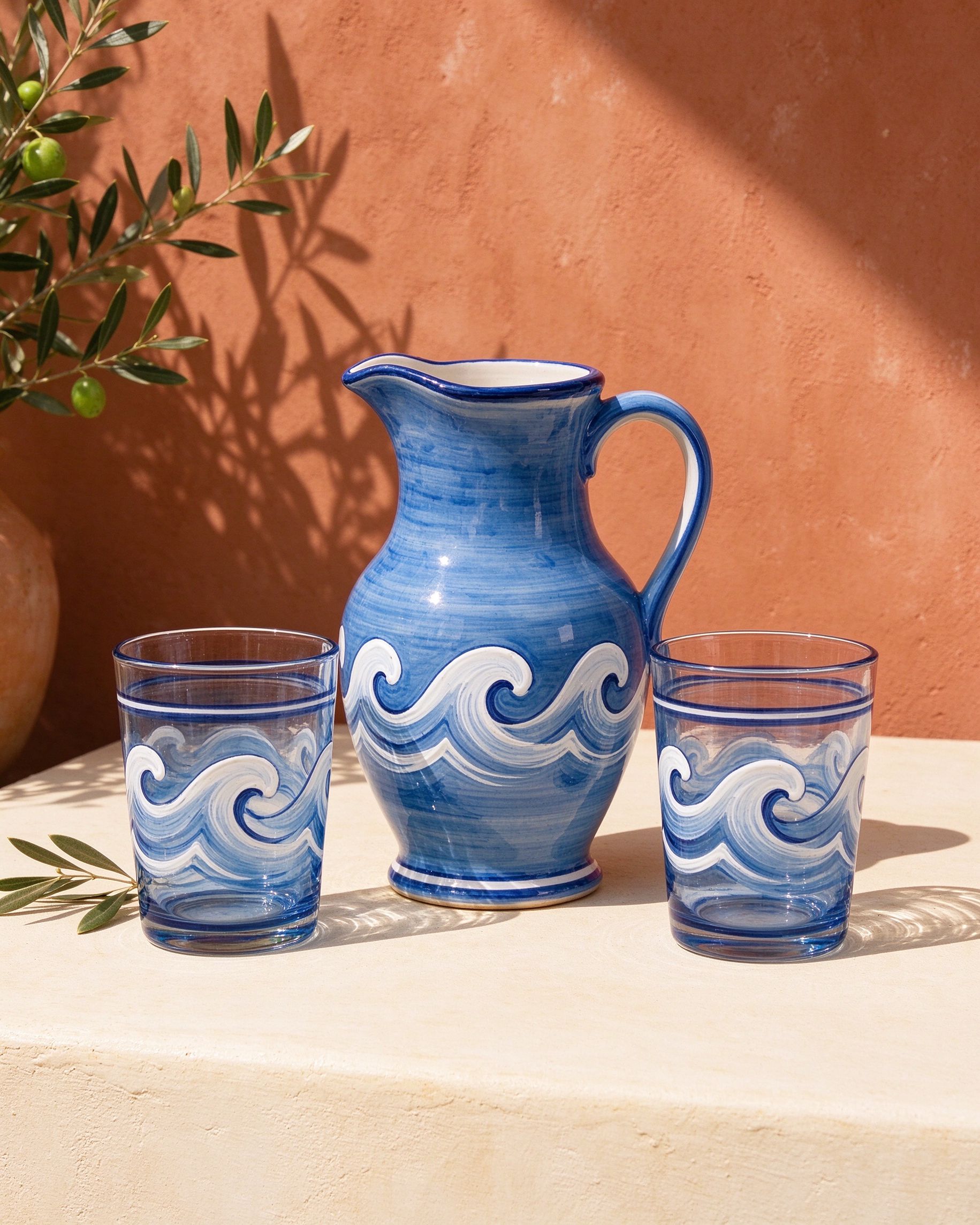 Hand-painted azure ceramic pitcher and two glasses with white wave motifs